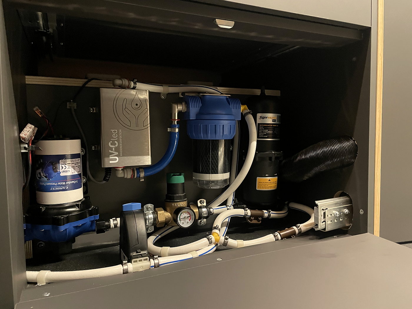Wasserinstallation hinter einer Möbelklappe: Pumpe, Filter und Leitungen, sauber verlegt