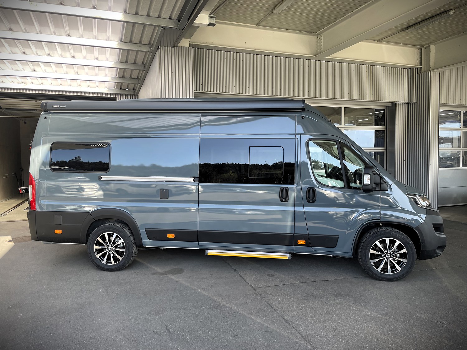 Graublauer Fiat Ducato mit ausgefahrener Markise vor einer Halle