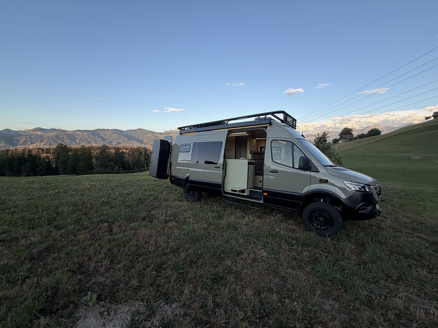 Sprinter-Ausbau mit geöffneter Schiebetür auf einer Wiese vor den Bergen